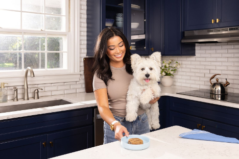 Smiling woman holding a West Highland White Terrier beside a bowl of wet food