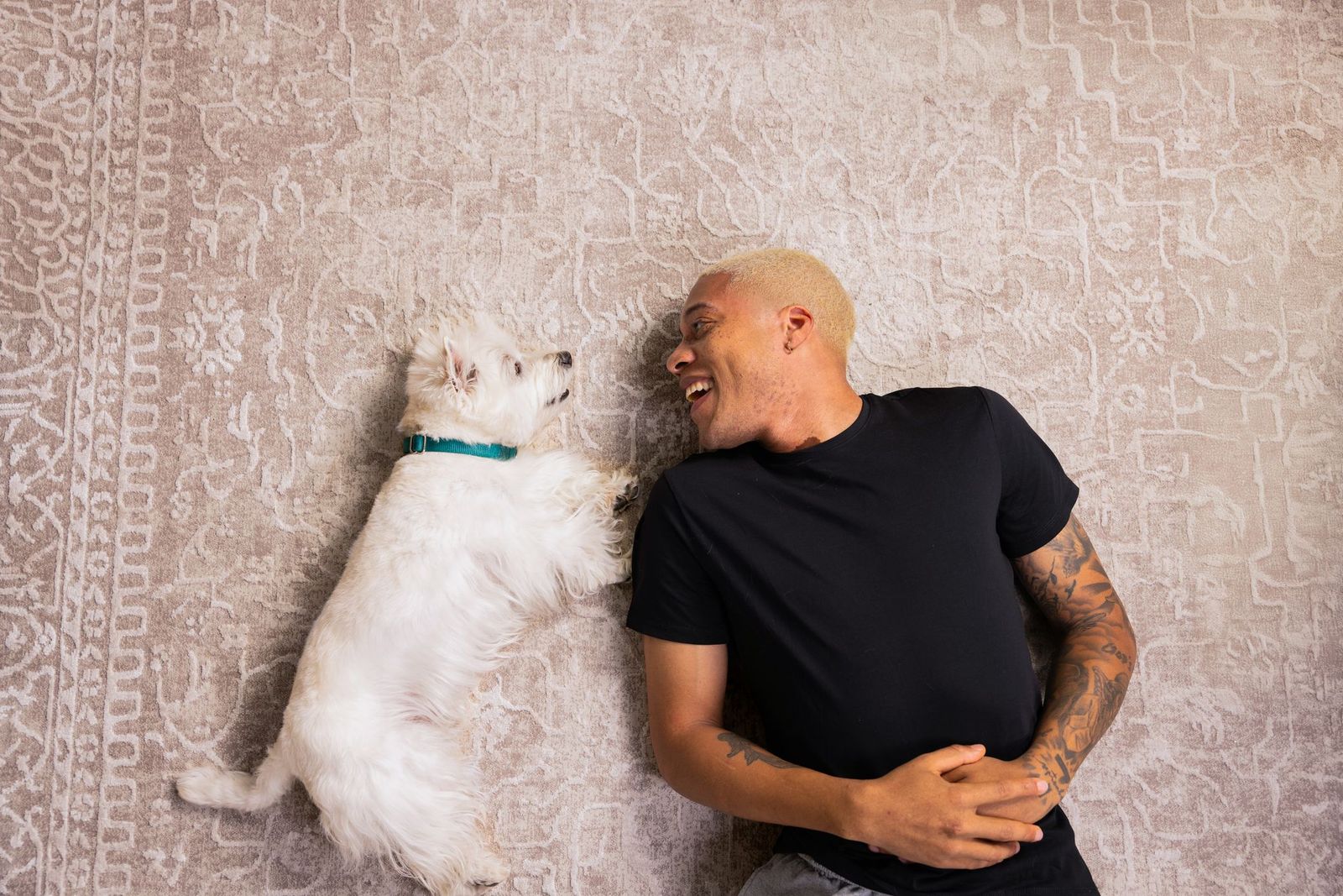 Man and Westie lying on a rug, facing each other